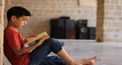 A young boy holds a Mushaf and recites Qur'an.